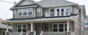 Two-story gray duplex house with two front porches, white trim, and multiple windows on each level.