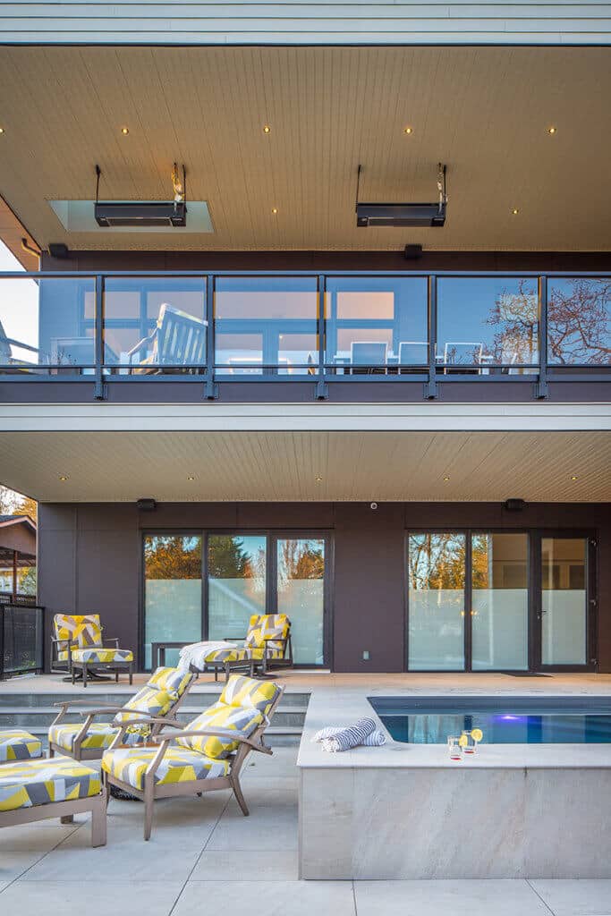 Modern Custom Home featuring a spacious outdoor patio with lounge chairs, a swimming pool, and large glass windows, showcasing a contemporary architectural design.