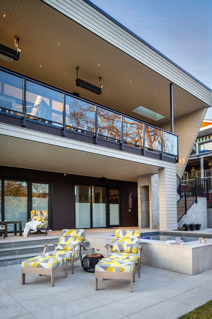 Modern Custom Home exterior featuring a spacious balcony, large windows, and stylish outdoor seating near a hot tub, showcasing contemporary design elements.