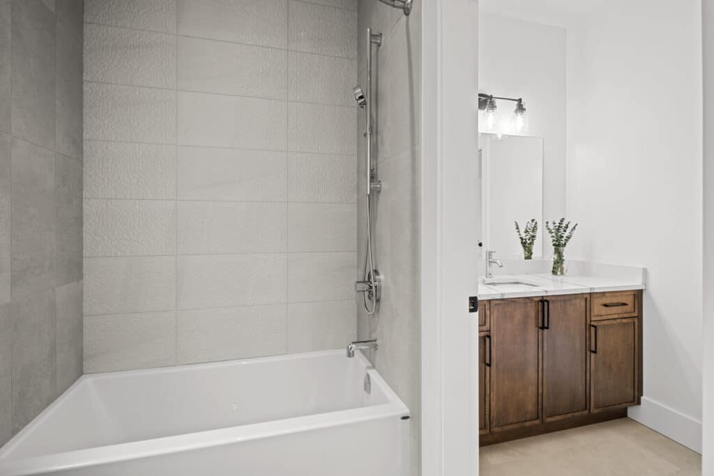 Modern bathroom with a white bathtub, tiled wall, shower fixture, wooden vanity with double sinks, and a large mirror above.