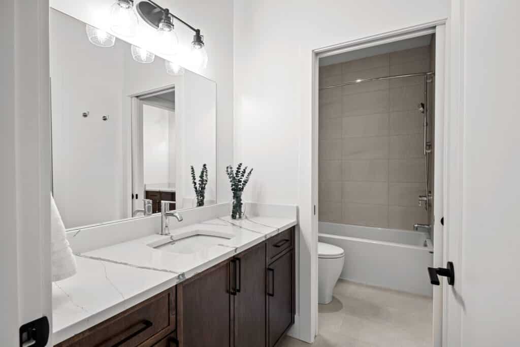 Modern bathroom with a large mirror, double sink vanity, dark wood cabinets, and a separate area with a bathtub and toilet.