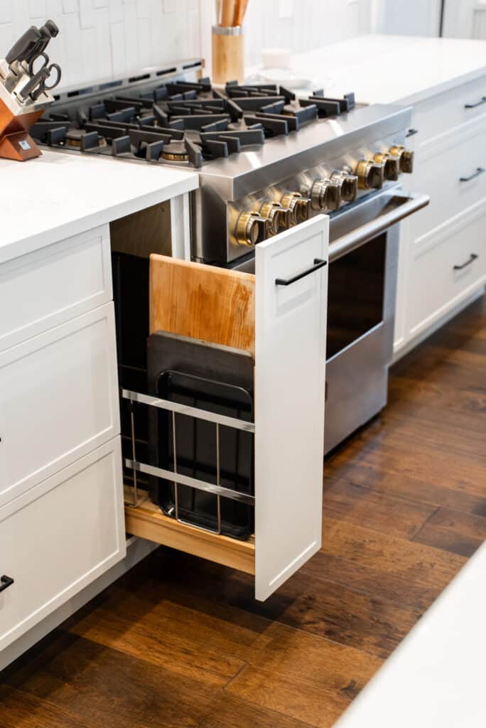 A kitchen features a stainless steel stove and oven, with a pull-out cabinet storing cutting boards and baking trays next to it.