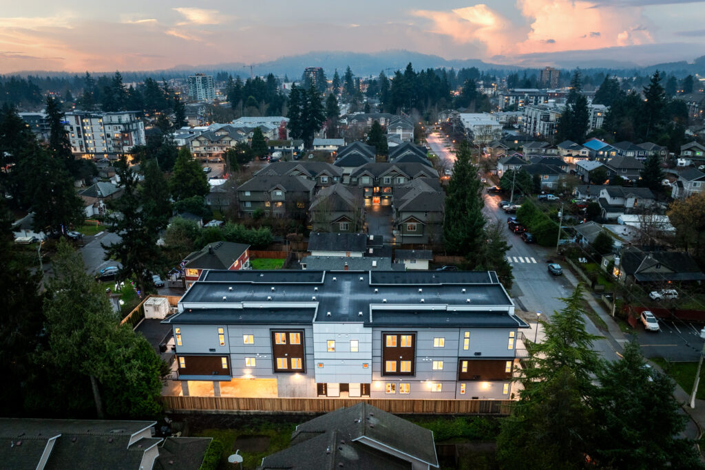 Aerial view of a modern Custom Home surrounded by a suburban neighborhood at dusk, showcasing contemporary architecture and well-lit exterior.