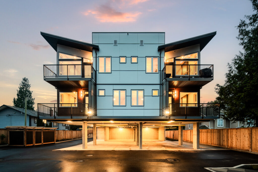 Modern Custom Home featuring a unique architectural design with large windows and multiple balconies, illuminated at sunset. The structure stands on stilts, providing covered parking space underneath. Ideal for showcasing contemporary living.